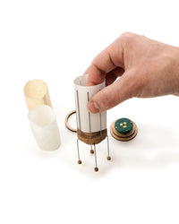 Hand holding a cylindrical wooden lamp with a white handle on a white background